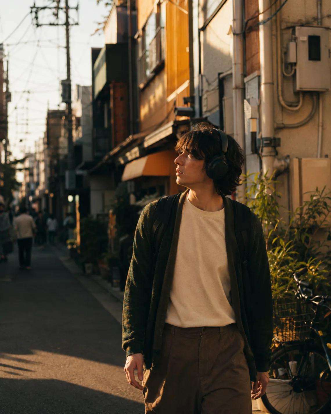A traveller walking a Tokyo backstreet at golden hour, headphones on, looking up at something off-frame